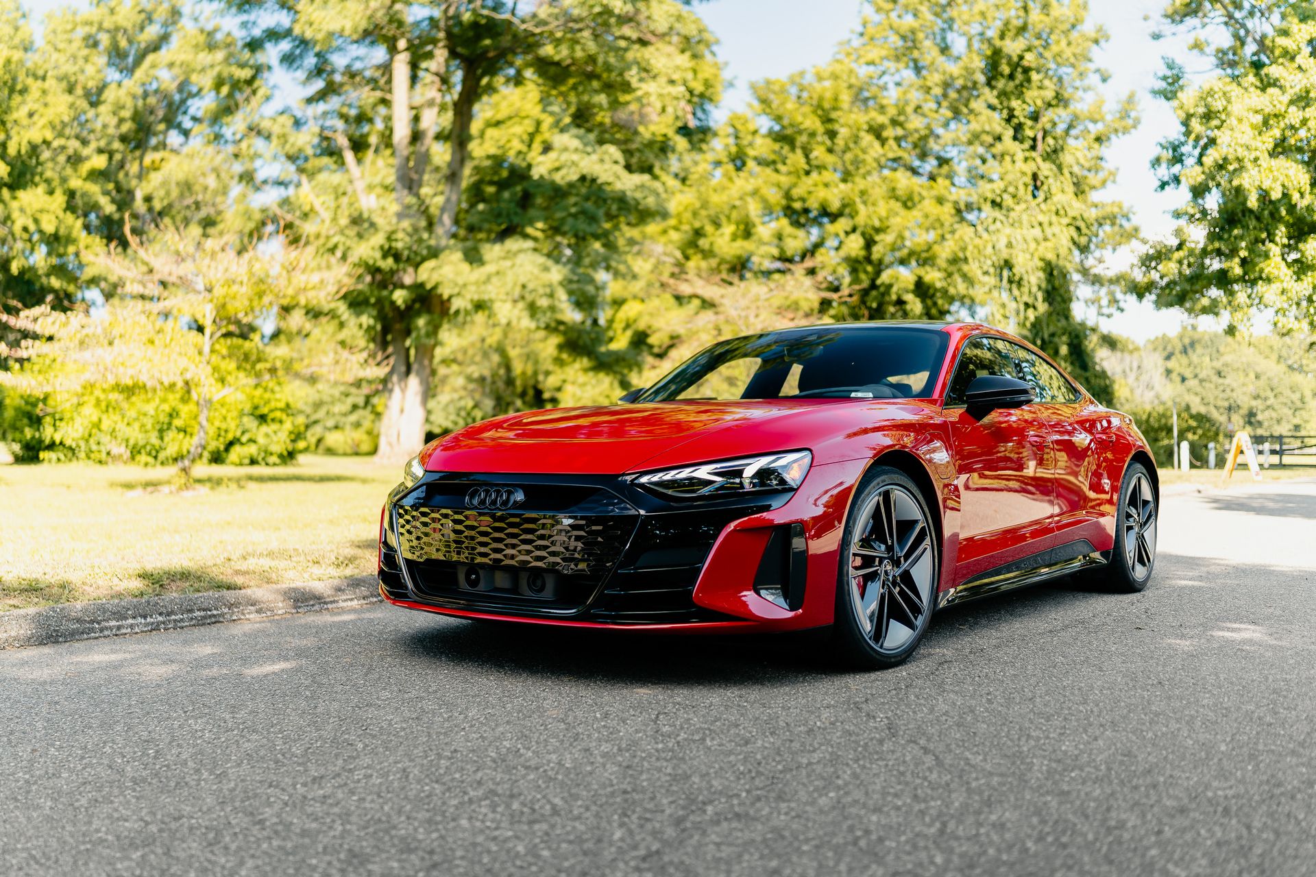 A sleek red electric car parked on a sunlit road surrounded by lush greenery.