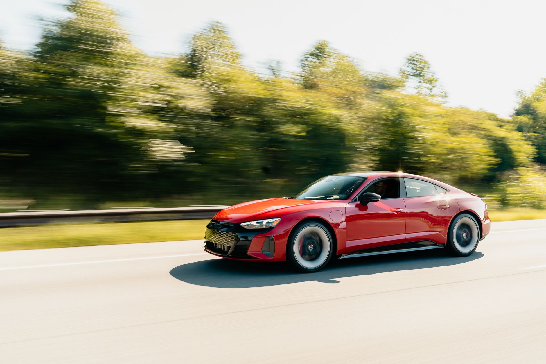 A sleek red coupe driving fast on a highway surrounded by blurred trees.