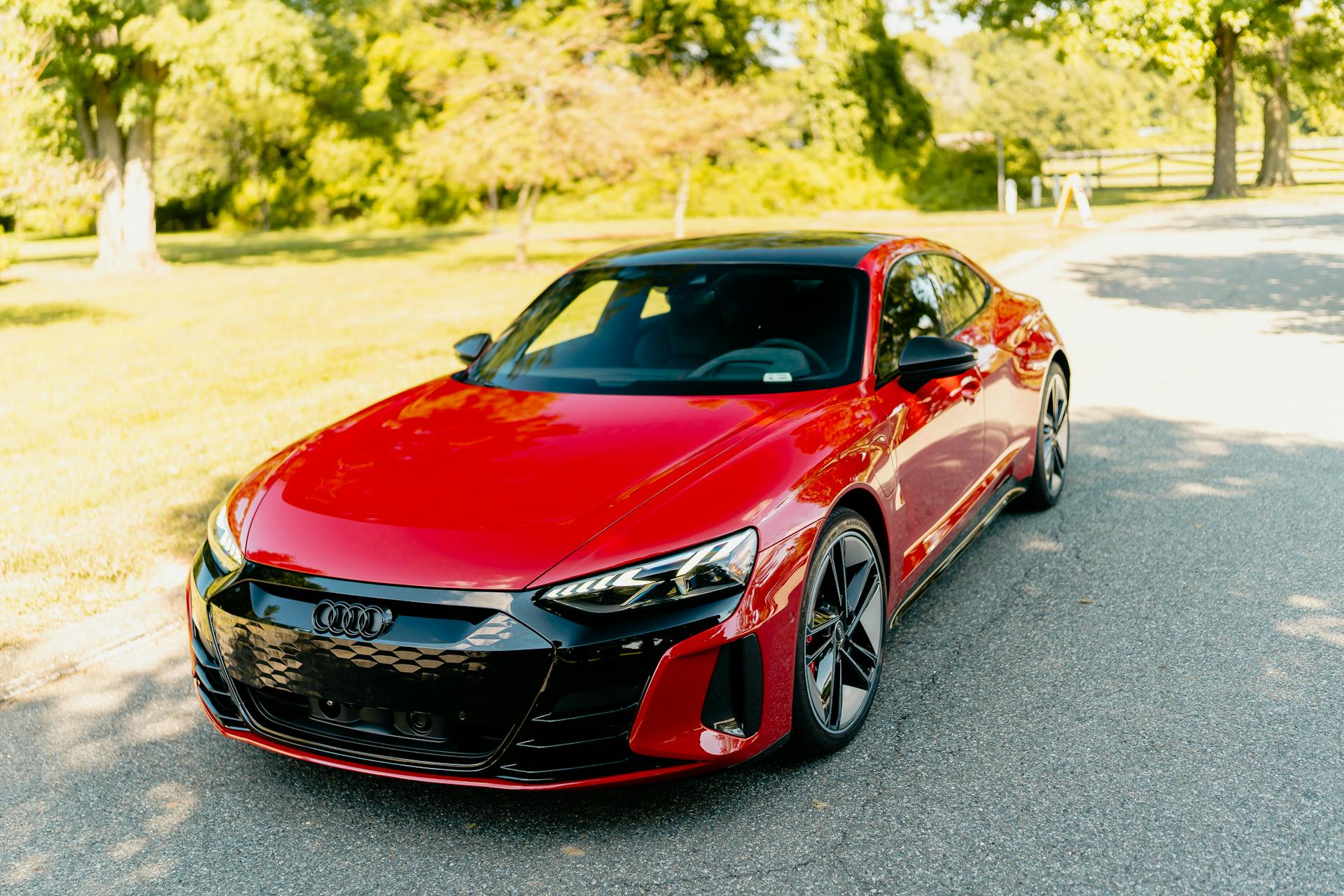 A sleek red luxury electric car parked under bright sunlight on a paved road.