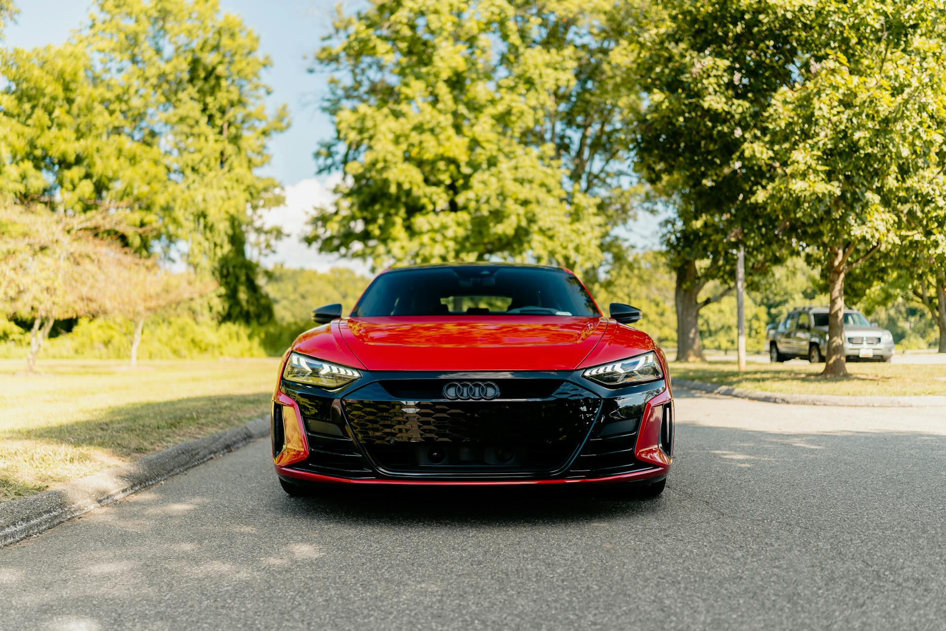 Front view of a sleek red Audi electric car parked on an outdoor road surrounded by greenery.