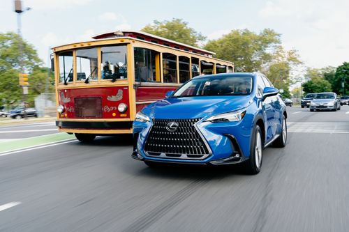 Free A blue Lexus driving alongside a vintage trolley in a bustling urban street setting. Stock Photo