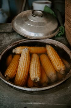 Fresh corn cobs steaming in a rustic kitchen setting, highlighting traditional cooking methods.