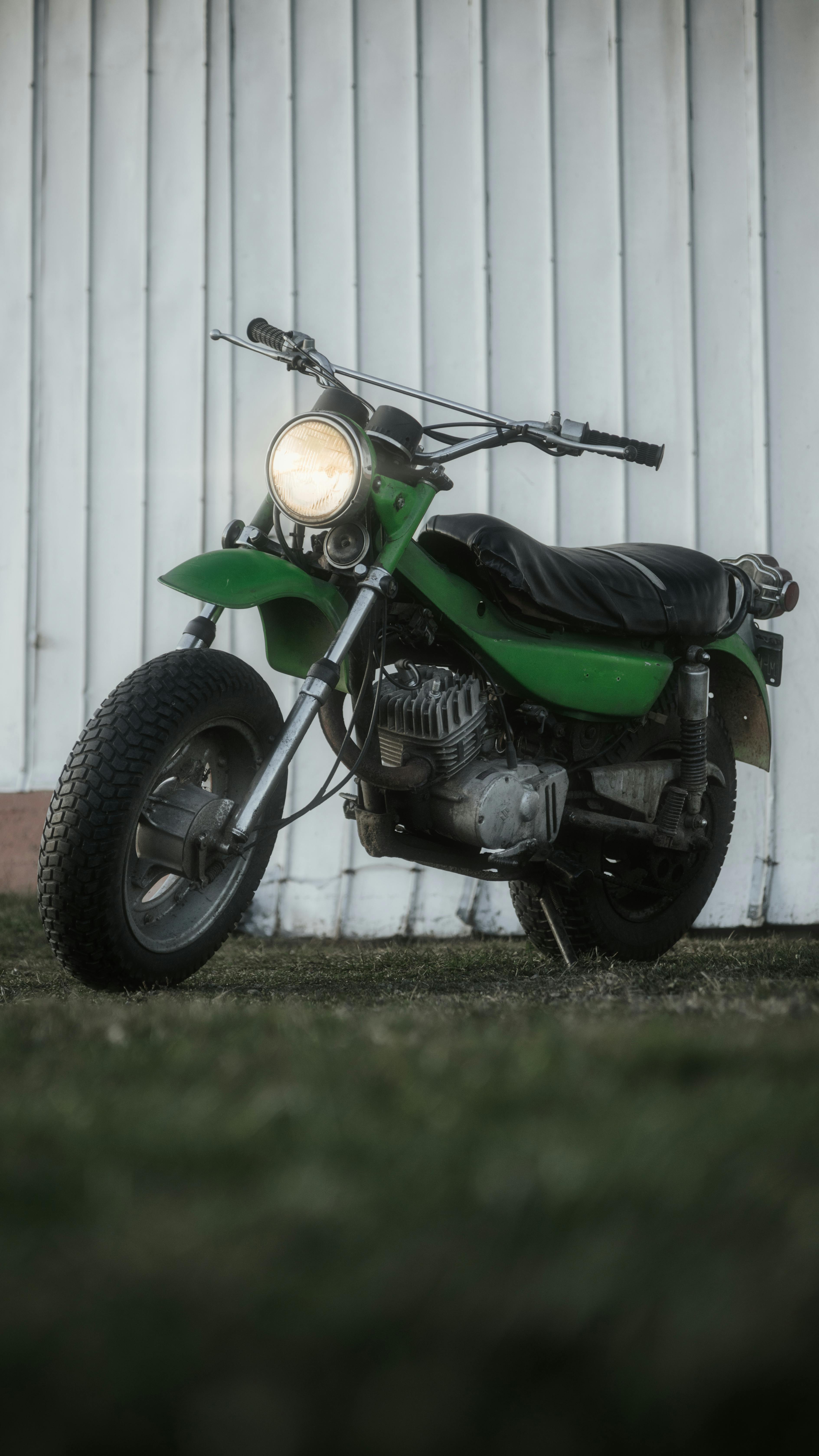 A classic green vintage motorcycle parked outside against a wooden wall.