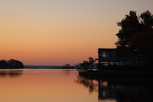 Free Peaceful view of a lakeside at twilight in Stamford, CT, highlighting calm waters and a silhouetted house. Stock Photo