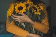 一位穿着芥末色毛衣的女人手持一束向日葵，散发着温暖舒适的氛围