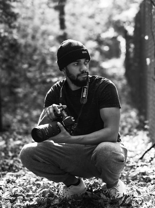 Grayscale Photo of Man Holding Camera While Crouching