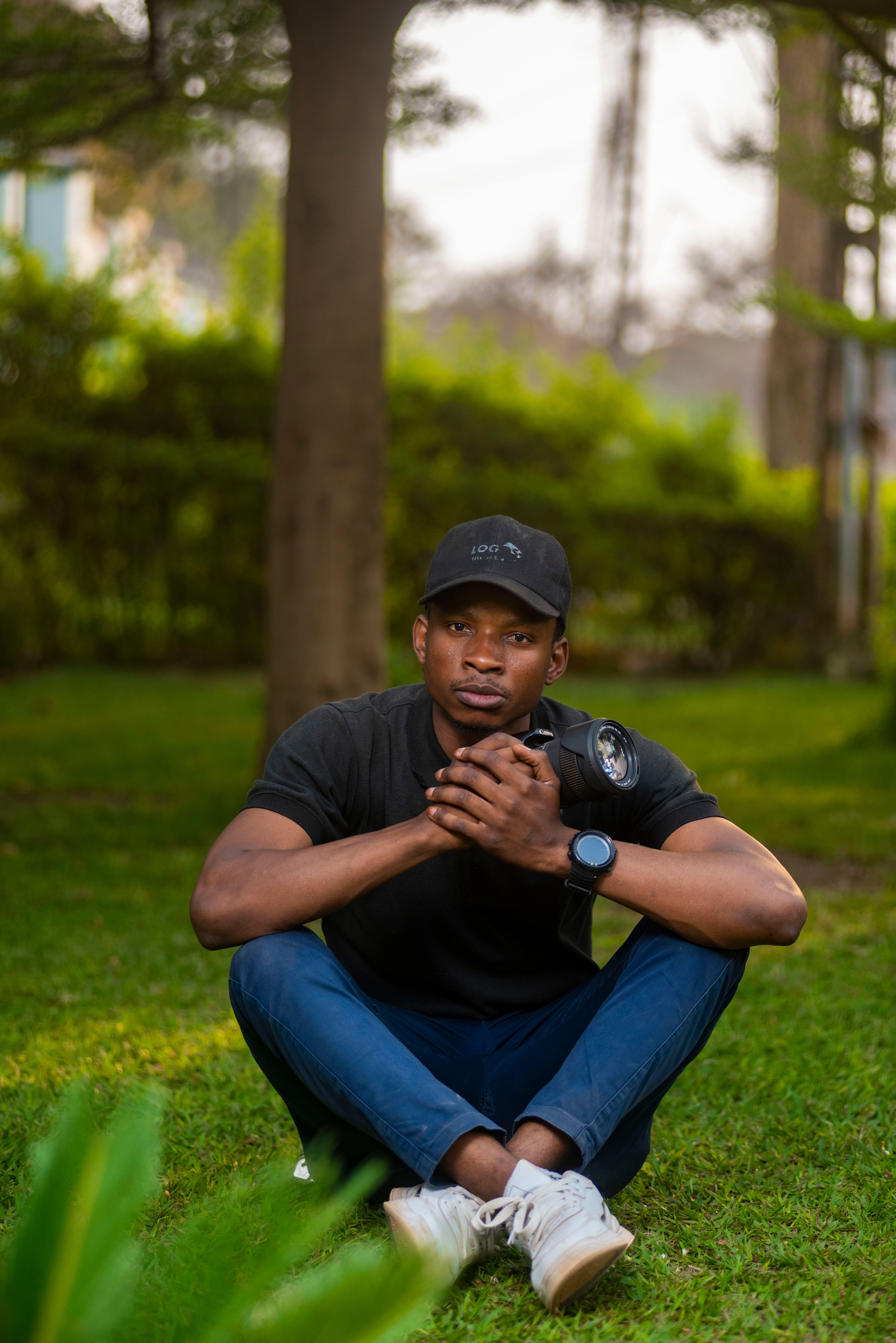 A photographer sits on grass with a camera, surrounded by nature in a park.