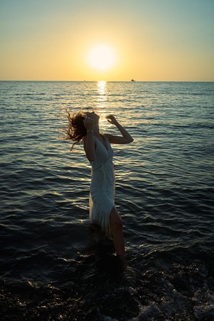 A woman enjoys the serene beauty of a sunrise by the sea, captured in silhouette.