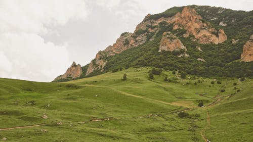 Green Grass Field on Brown Mountain Under White Sky