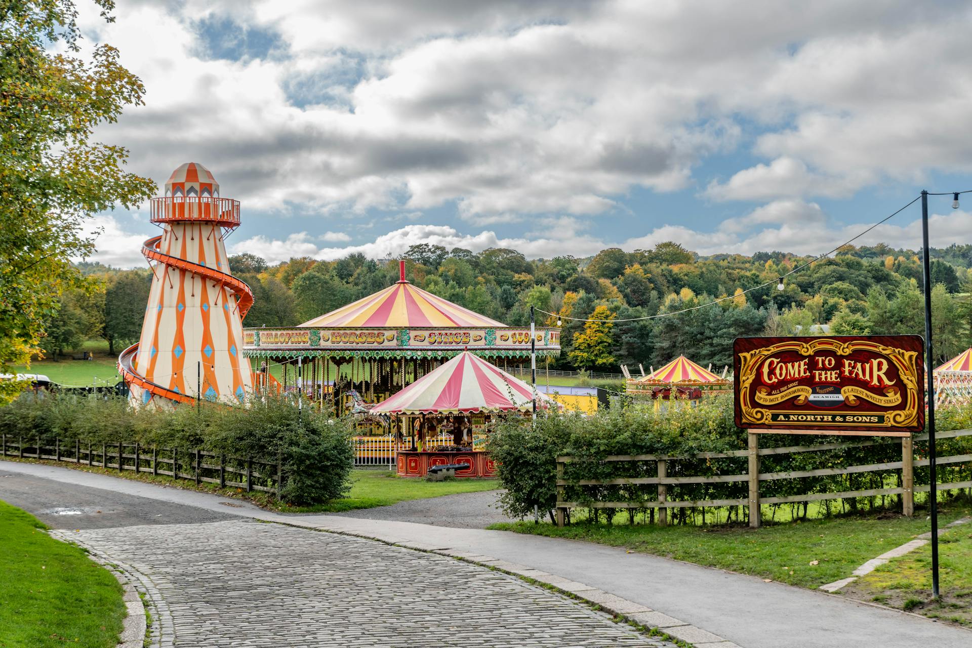 Vibrant scene of a traditional fairground with a carousel and helter skelter under a cloudy sky.