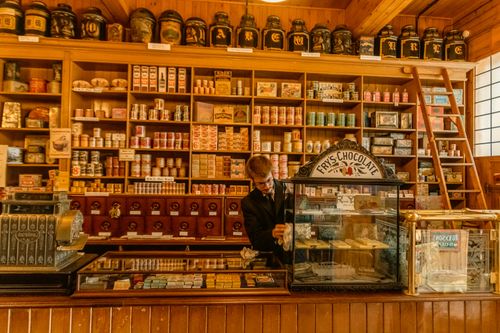 Free A vintage chocolate shop interior with wooden shelves and a seller arranging products. Stock Photo