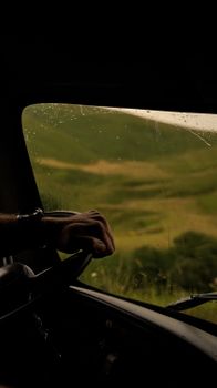 Hand on steering wheel inside vehicle during rainy drive through Russian mountains near Elbrus.