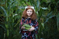 一位迷人的年轻女孩手拿玉米，站在郁郁葱葱的玉米地里，展现了收获季节与乡村生活的本质