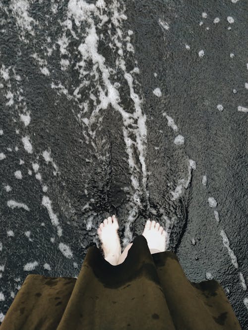 Person Standing Barefoot on a Black Sand Beach 
