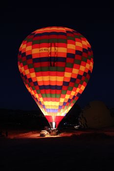 Vibrant hot air balloon glowing at night in Cappadocia, Turkey, under a starry sky.