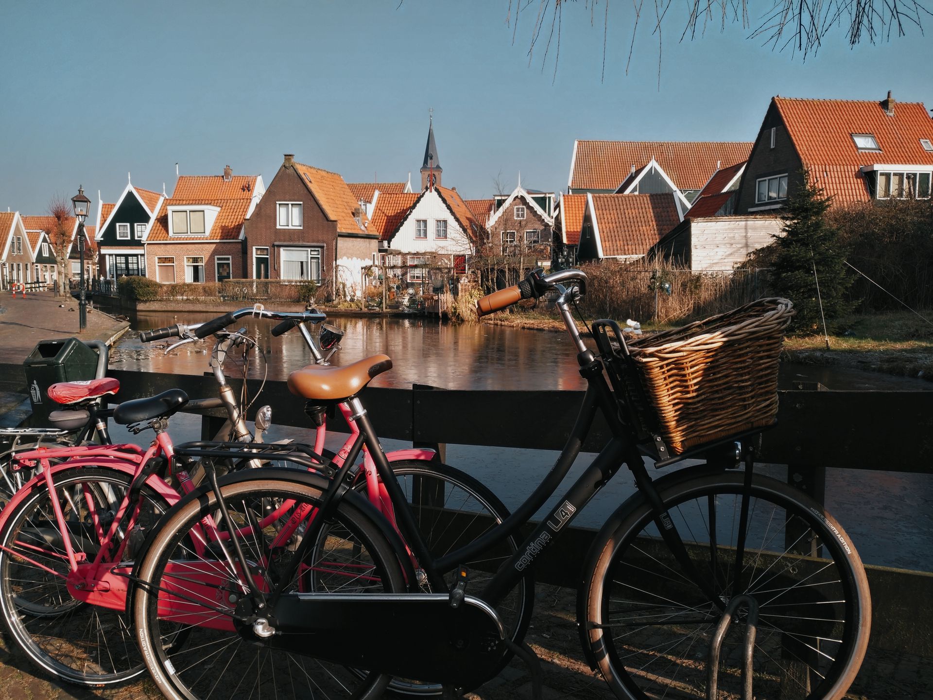 Sunny day in Amsterdam with bicycles near a canal, displaying typical Dutch houses and serene urban life.