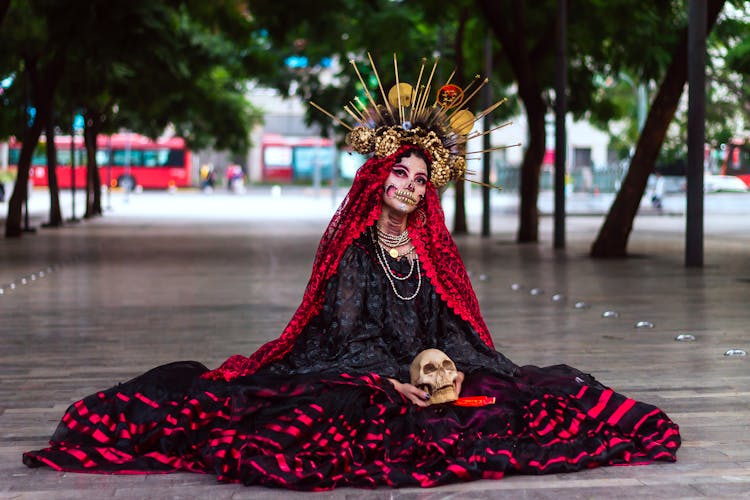 Woman In Face Paint And Crown Sitting On Ground Holding Skull