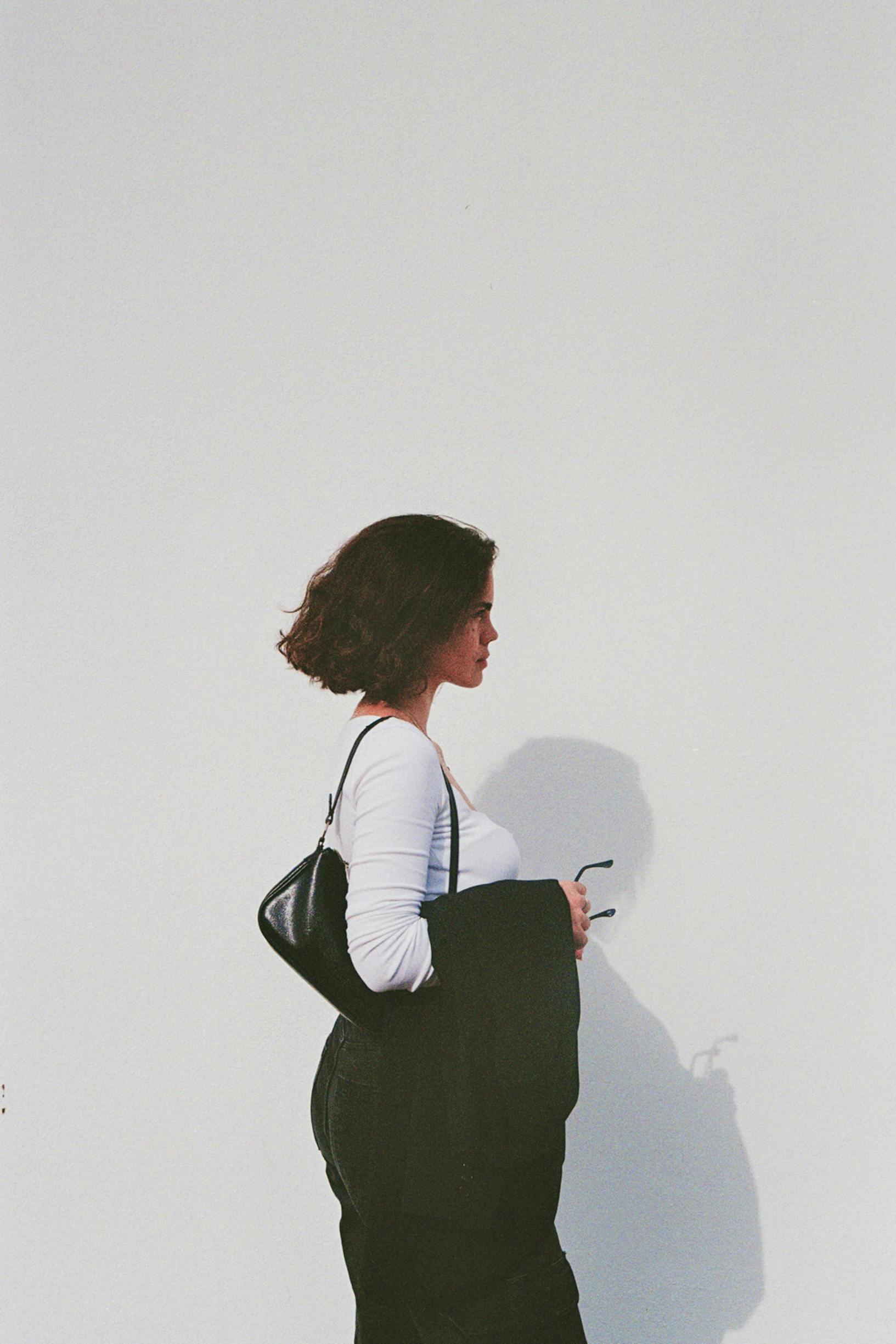 A stylish woman in monochrome outfit poses confidently against a white backdrop, exuding modern elegance.