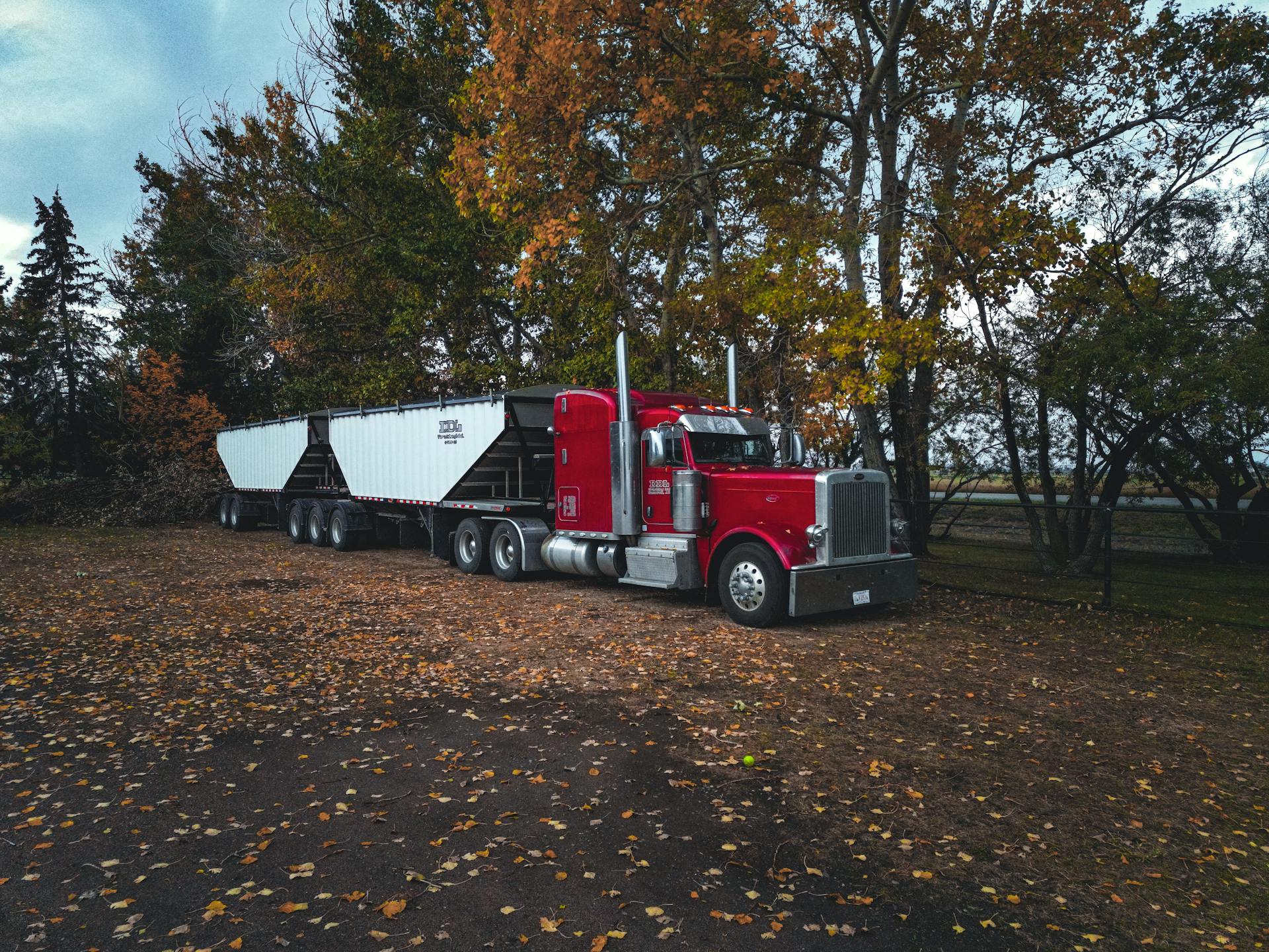 A red trailer truck parked outdoors surrounded by autumn trees in Purple Springs, Canada.