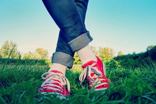 Stylish jeans and red sneakers captured in an outdoor grassy setting, showcasing casual fashion.