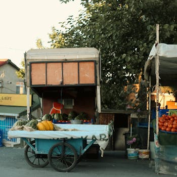 Street market stall with colorful vegetables and an old cart in an outdoor setting.
