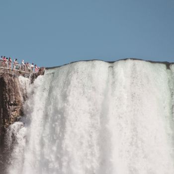 Tourists overlooking the majestic Niagara Falls under a clear blue sky.