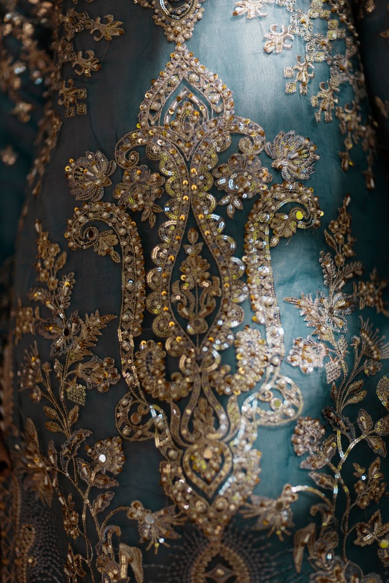 Close-up of ornate golden embroidery on rich teal fabric, showcasing exquisite craftsmanship