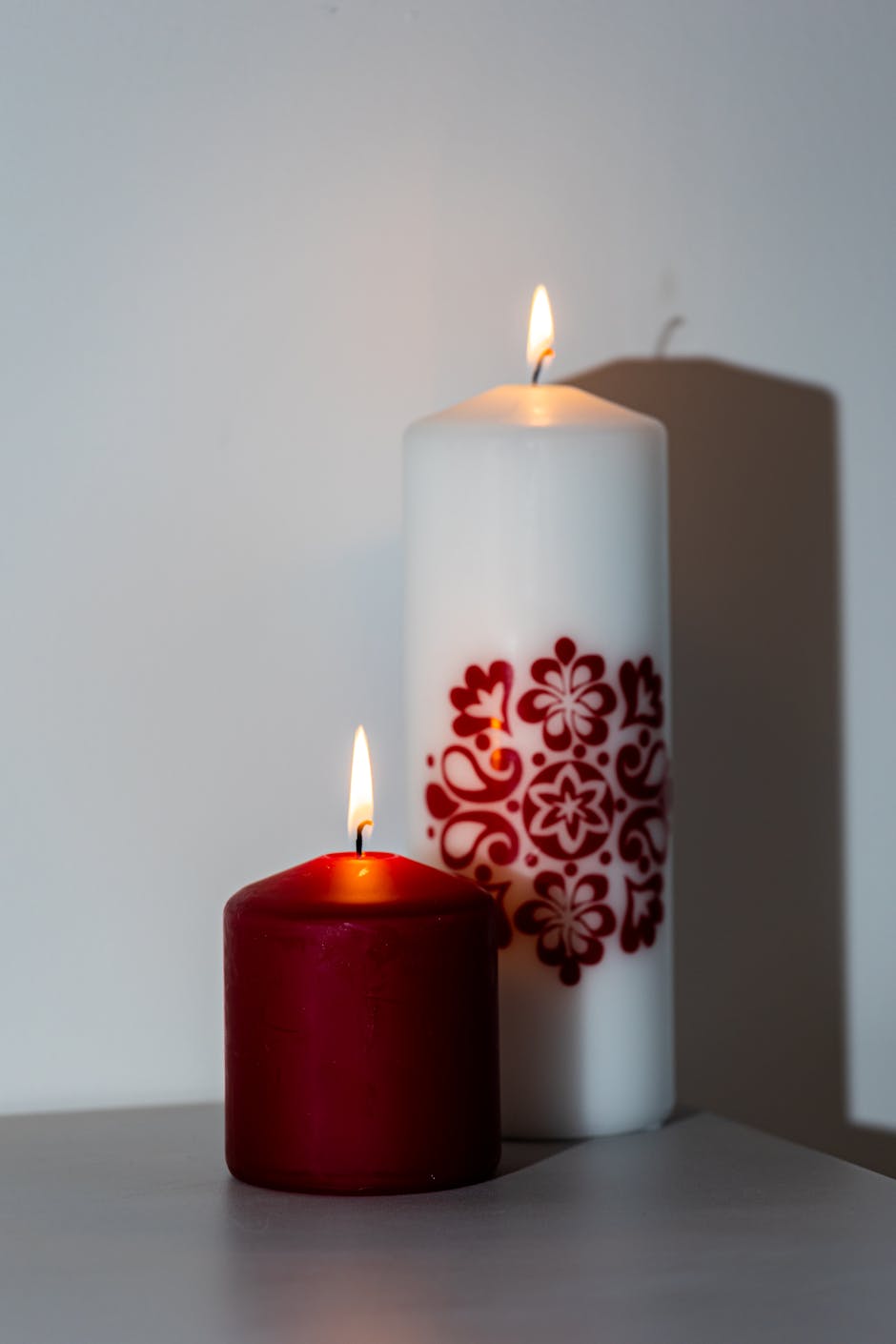 Two candles illuminated in a warm glow, featuring decorative red patterns on the white candle.