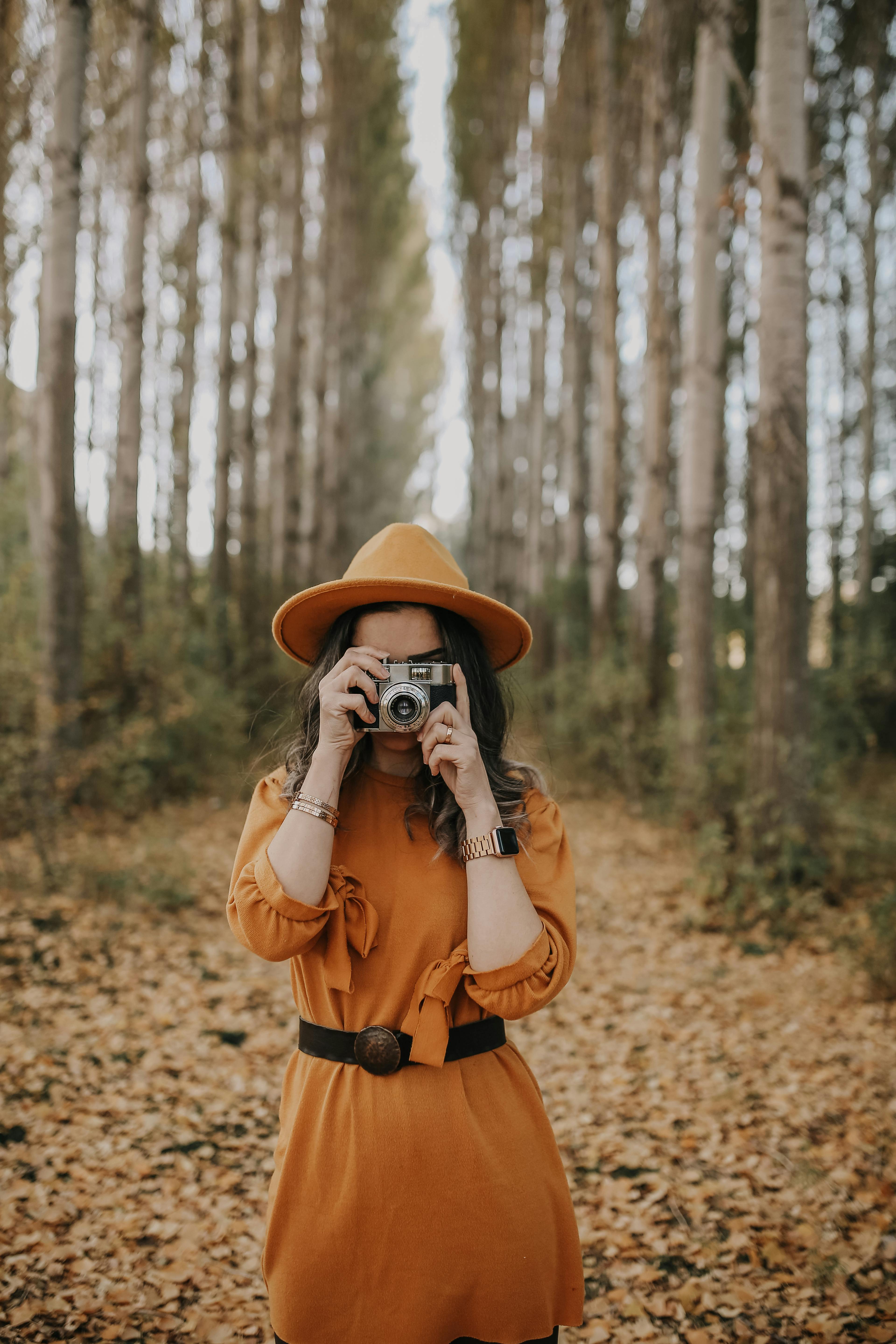 Woman in stylish autumn outfit photographing in a leafy forest.