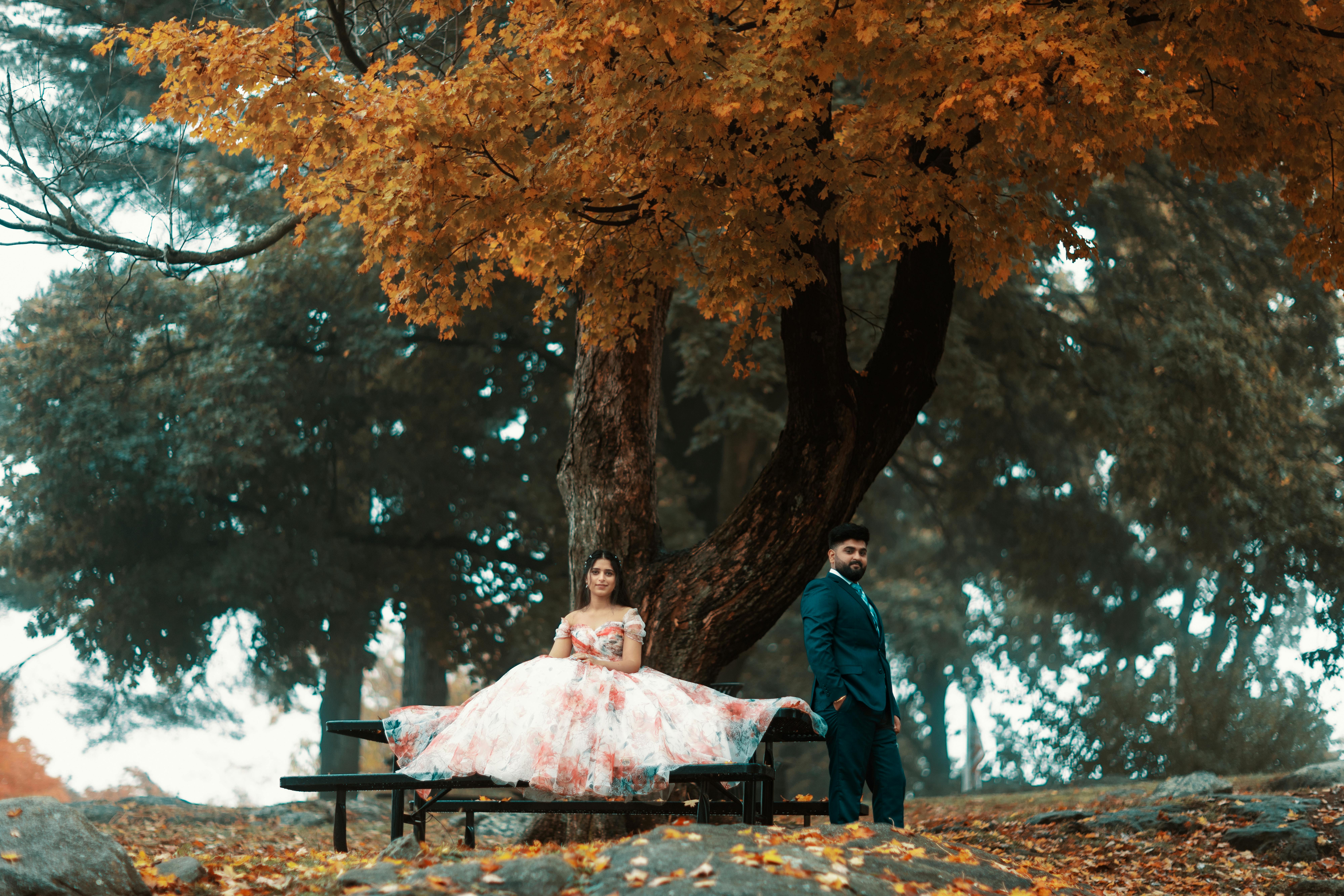 A romantic couple in wedding attire under a colorful autumn tree.