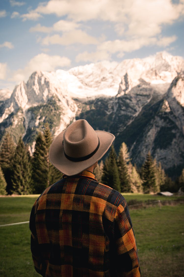 Back View Of A Man In A Hat Looking At A Mountain Range 