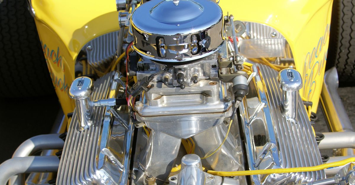 Detailed view of chrome engine parts in a yellow vintage car, showcasing mechanical intricacy.