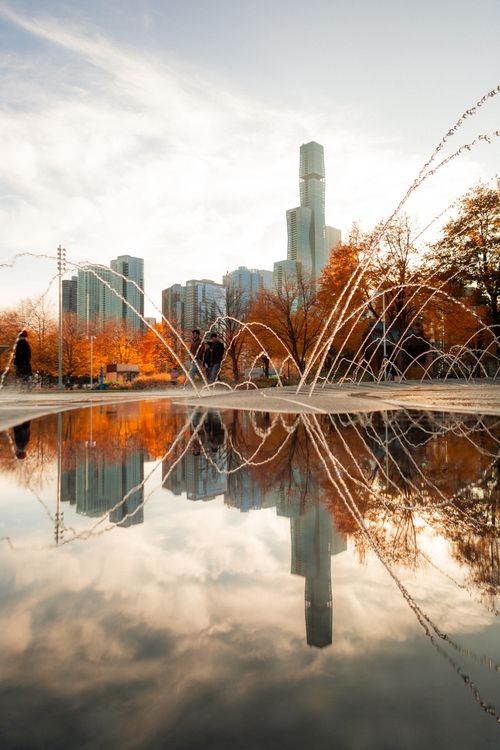 Free Skyscrapers and fountains reflecting in autumn park pool, capturing city serenity. Stock Photo