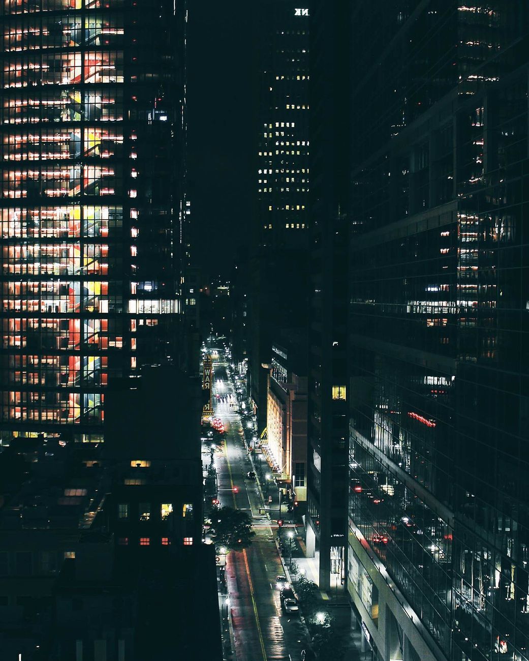 A vibrant nighttime cityscape featuring illuminated skyscrapers and busy streets in an urban area.