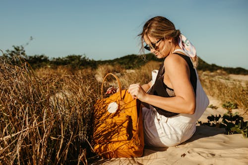 Young Woman with a Yellow Backpack Sitting on a Beach