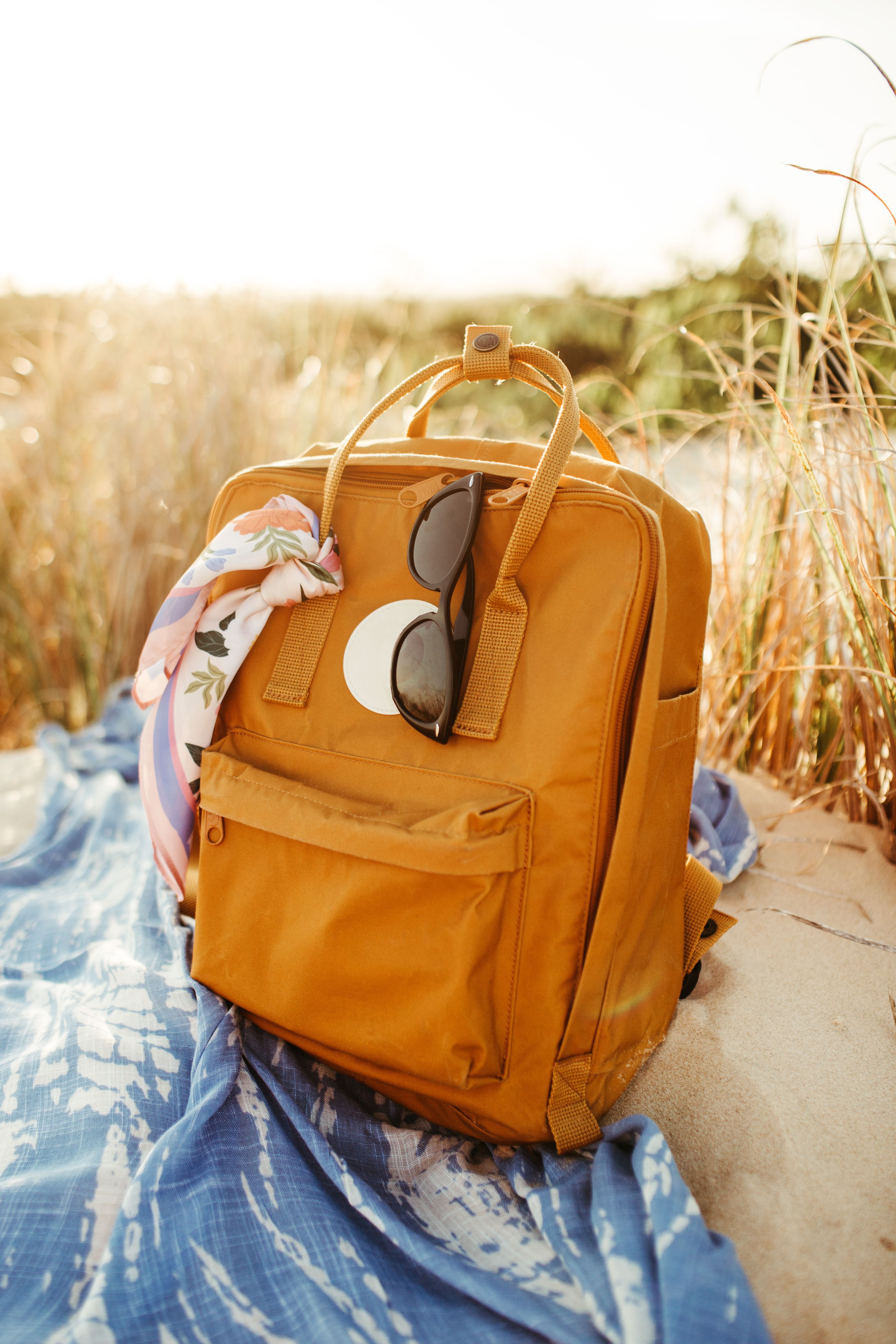 Mochila laranja estilosa com óculos de sol descansando em uma toalha de praia sob a luz do sol de verão.