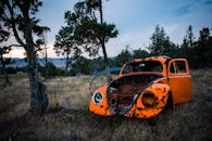 一辆生锈的废弃大众甲壳虫汽车停放在风景优美的户外，四周树木环绕