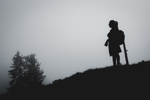 Silhouette of Woman with Backpack Standing on Mountain Hill