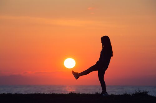 Free Dramatic sunset silhouette of a woman playfully interacting with the sun by the sea. Stock Photo