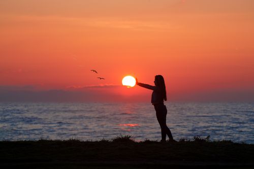 Free A woman silhouetted by the sunset, standing by the ocean, creating a tranquil seaside scene. Stock Photo