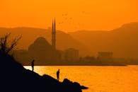 在科根充满活力的日落中，清真寺和人物的剪影与飞鸟相伴