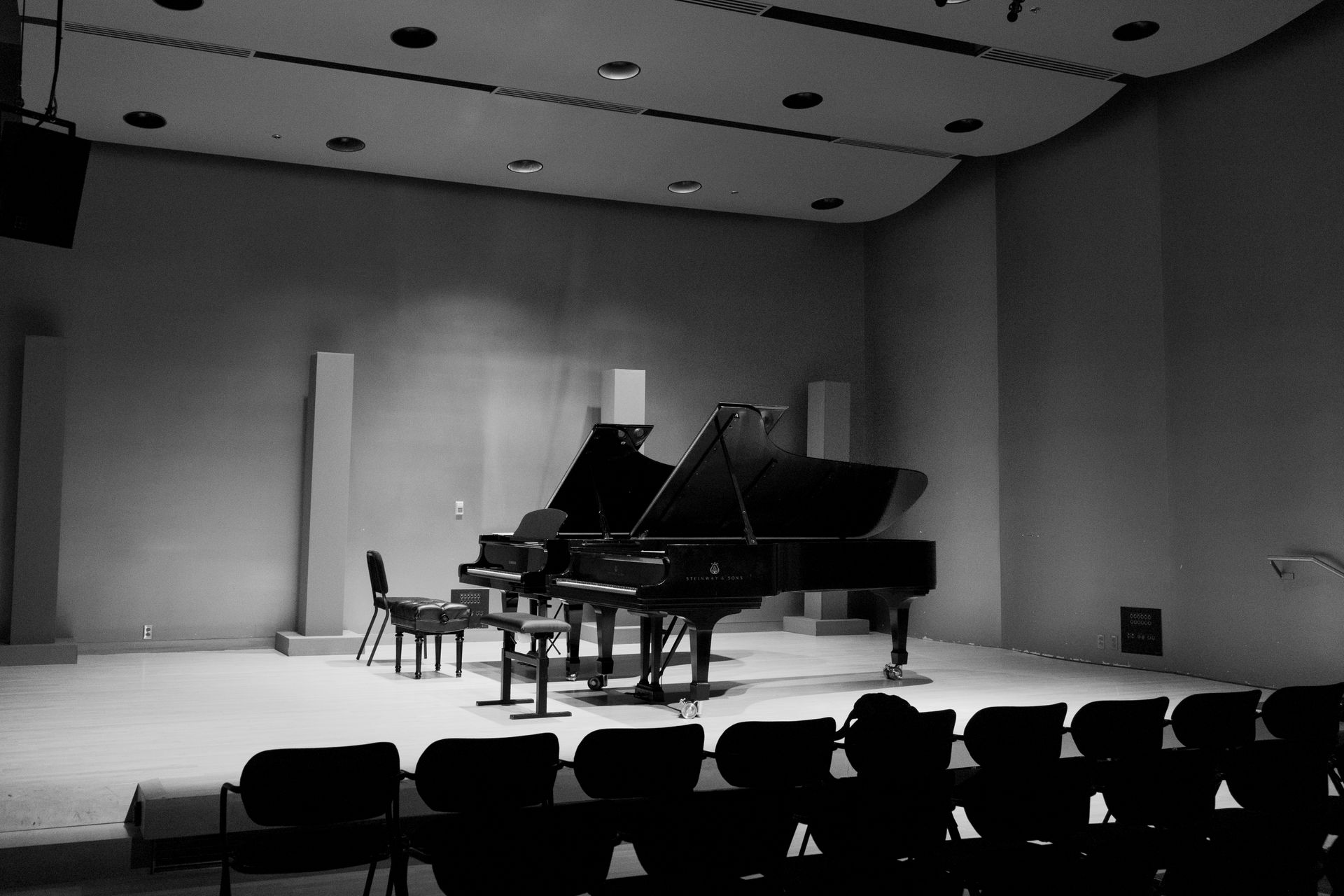 Loş ışık altında bir konser sahnesinde duran kuyruklu piyano.