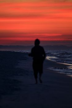 A person runs along a beach at sunset, creating a vibrant silhouette against an orange sky.