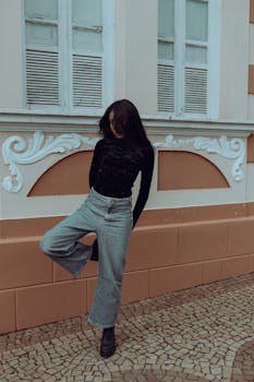 Fashionable woman posing in urban setting with ornate architecture.