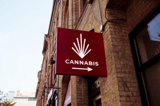 A red sign featuring a cannabis emblem on a city building facade, indicating a store direction.