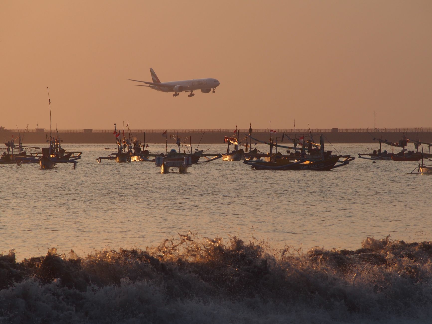 Commercial airplane flying over boats at sunset in Denpasar, Bali, Indonesia.