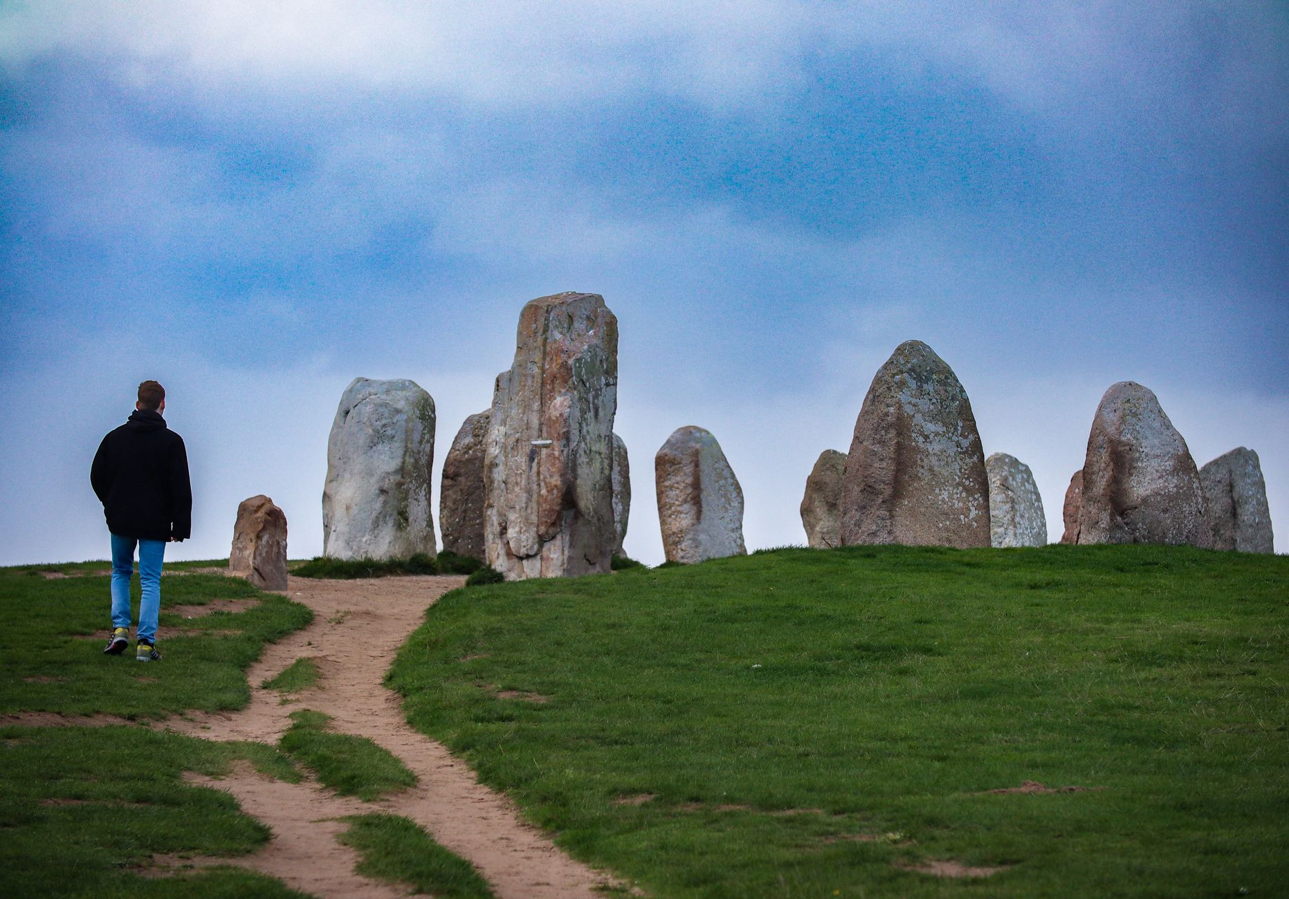 A lone figure walking towards a historic stone circle in Skåne, reflecting ancient times.