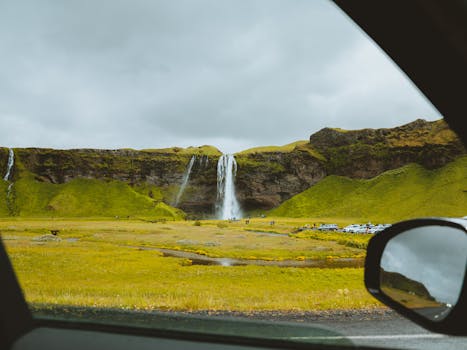 Capture of Seljalandsfoss waterfall in Iceland, seen through a car window with vibrant green landscapes.