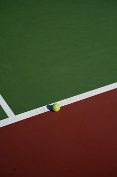 Close-up of a tennis ball on a vibrant green and red outdoor court, showcasing sport and leisure.