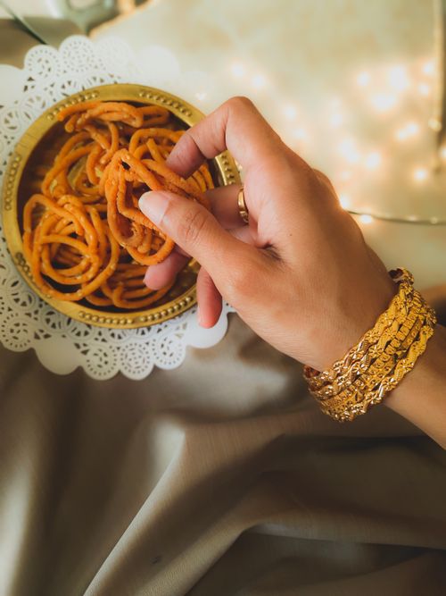 Free Hand adorned with gold bracelets picking Indian snack from a doily-lined bowl. Stock Photo